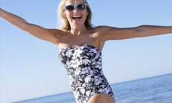 Picture of a woman, happy with her abdomen liposuction procedure she had with Top Plastic Surgeons in beautiful Cabo San Lucas, Mexico.  The woman is facing the camera with arms outstretched and running through the surf on a beach.