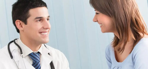 Picture of a smiling patient consulting with a smiling plastic surgeon in Cabo San Lucas, Mexico.  The patient is wearing a light blue shirt and the doctor is wearing a white smock