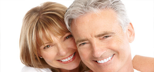 Close-up picture of a smiling couple looking directly into the camera showing their happiness with  the plastic surgery they had done in Cabo San Lucas, Mexico.  The woman has medium brown hair and the man has white hair.