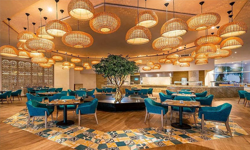 Picture of an elegant hotel lobby in Cabo San Lucas, Mexico.   The picture shows an ornate ceiling with golden lighting and blue tables and chairs.