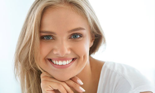 Picture of a beautiful woman, happy with her face lift procedure in Cabo San Lucas, Mexico.  The woman has long blonde hair, is looking directly into the camera and is holding her right hand to her chin highlighting her face lift.