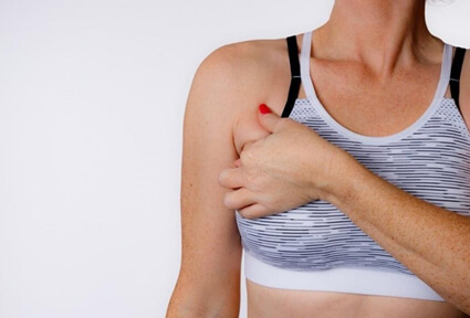 Picture of a woman facing the camera and happy with the perfect bra line liposuction procedure she had with top plastic surgeons in beautiful Cabo San Lucas, Mexico.  The woman is wearing a soft light purple pastel top and holding one hand to the area of her bra line liposuction.