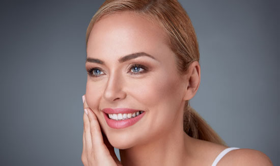 Picture of a woman, facing the camera and happy with her perfect face lift with neck lift procedure she with Cabo MedVentures in beautiful Cabo San Lucas, Mexico.   The woman has her hand to the side of her face indicating her happiness with the face lift with neck lift.