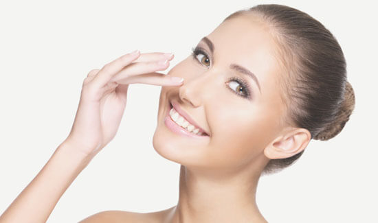 Picture of a woman, facing the camera and happy with her perfect nose surgery procedure she had with Cabo MedVentures in beautiful Cabo San Lucas, Mexico.  The woman has her hand to the side of her nose and is pointing to where she had the surgery.