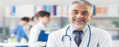 Picture of a plastic surgeon representing the doctors at Top Plastic Surgeons in Cabo San Lucas, Mexico.  The picture shows a doctor in a white coat with a stethoscope around his neck and arms crossed, looking directly at the camera and smiling.