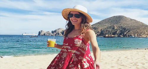 Picture of an attractive woman on a beautiful Los Cabos beach, enjoying a sunny day.  The woman has on a red and white dress with a beautiful blue Los Cabos sky in the background.